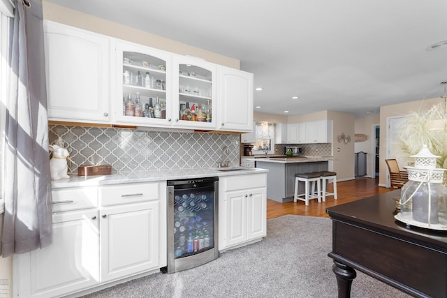 kitchen with a breakfast bar, beverage cooler, backsplash, white cabinets, and glass insert cabinets