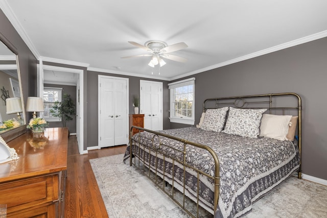 bedroom featuring multiple closets, ornamental molding, a ceiling fan, wood finished floors, and baseboards