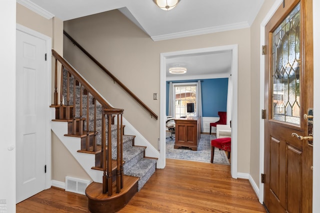 foyer entrance featuring visible vents, ornamental molding, wood finished floors, stairway, and baseboards