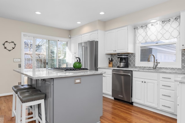 kitchen with a sink, a kitchen breakfast bar, wood finished floors, a center island, and stainless steel appliances