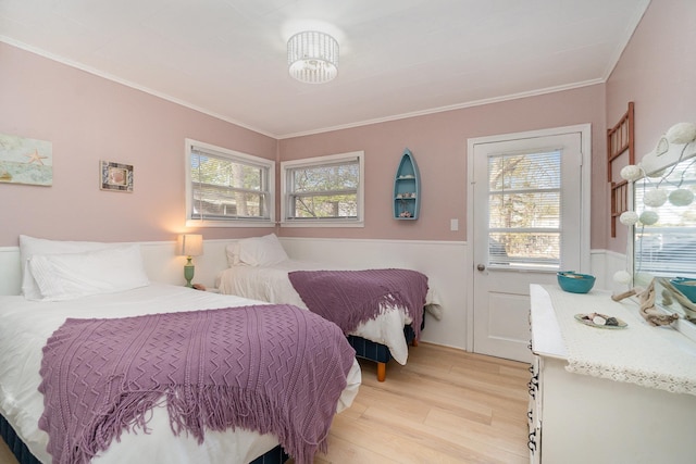 bedroom featuring multiple windows, light wood-style floors, ornamental molding, and wainscoting