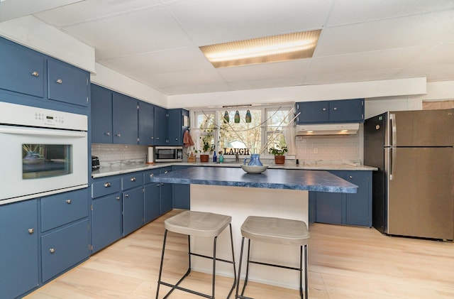 kitchen with blue cabinetry, stainless steel appliances, light wood-type flooring, and under cabinet range hood