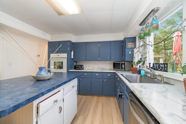 kitchen with blue cabinetry, light wood-style flooring, a sink, stainless steel appliances, and tasteful backsplash