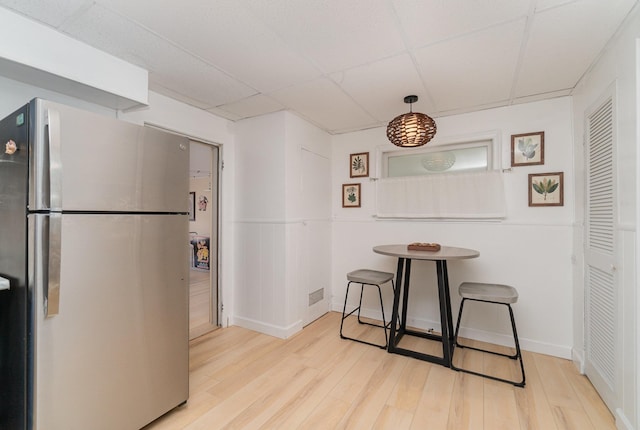 kitchen with a drop ceiling, freestanding refrigerator, visible vents, and wood finished floors