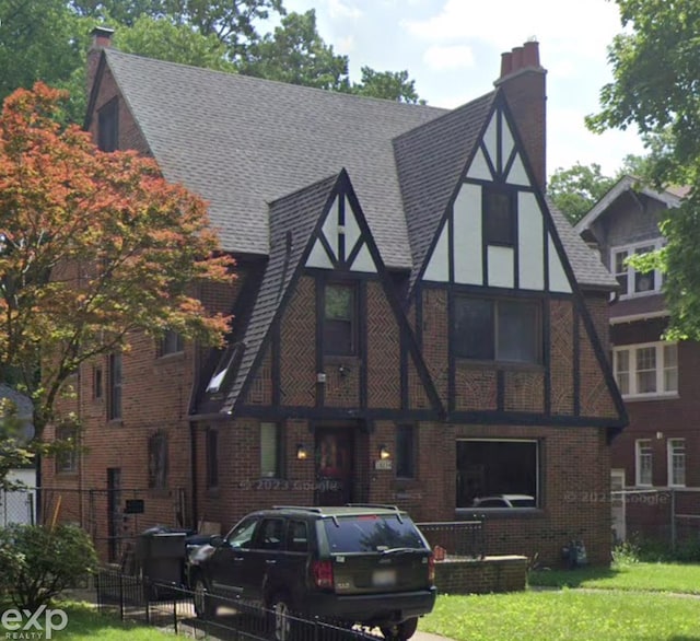 tudor house with brick siding, a shingled roof, a chimney, and fence