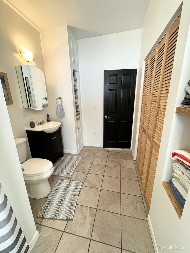 bathroom featuring vanity, toilet, baseboards, and a closet