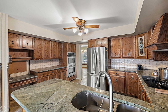 kitchen featuring a ceiling fan, custom range hood, a sink, stainless steel appliances, and decorative backsplash