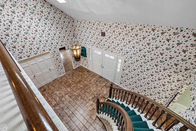 foyer featuring stairway, a textured ceiling, vaulted ceiling, and wallpapered walls