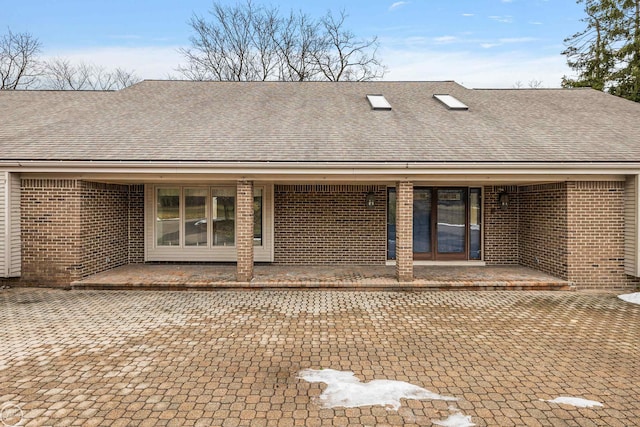 back of house featuring brick siding and a shingled roof