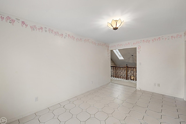 spare room featuring lofted ceiling with skylight, light floors, and baseboards