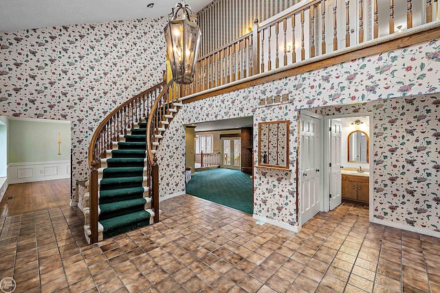 stairway with a chandelier, tile patterned floors, wallpapered walls, and a high ceiling