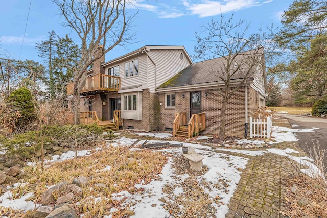 snow covered house featuring a balcony, brick siding, and a chimney