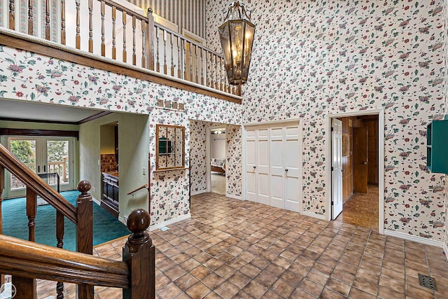 tiled foyer entrance with visible vents, baseboards, an inviting chandelier, and a towering ceiling