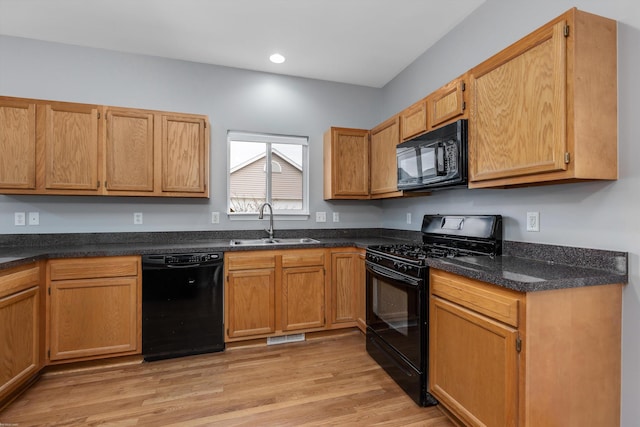 kitchen with dark stone counters, recessed lighting, light wood-style floors, black appliances, and a sink