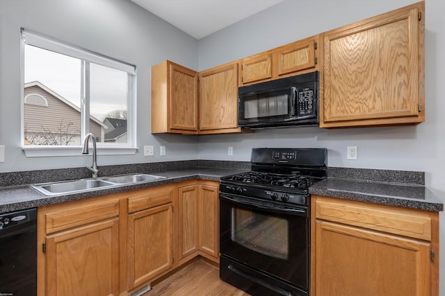 kitchen with black appliances, dark countertops, light wood-type flooring, and a sink