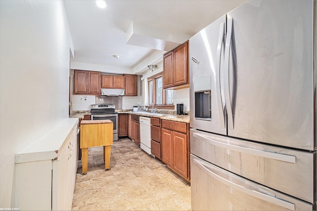 kitchen featuring brown cabinetry, a sink, stainless steel appliances, light countertops, and under cabinet range hood