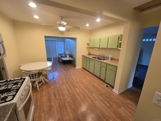 kitchen with green cabinets, ceiling fan, white gas stove, wood finished floors, and a sink