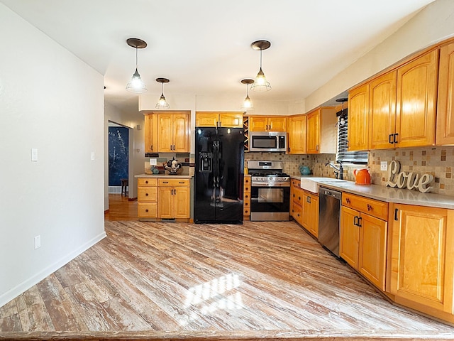 kitchen with a sink, light wood-style floors, appliances with stainless steel finishes, light countertops, and decorative backsplash