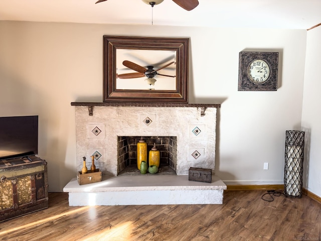 unfurnished living room featuring wood finished floors, a ceiling fan, baseboards, and a fireplace with raised hearth