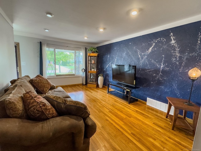 living room featuring wood finished floors, visible vents, baseboards, wallpapered walls, and an accent wall