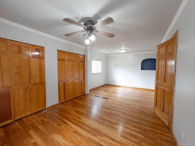 unfurnished bedroom featuring light wood-type flooring, multiple closets, a ceiling fan, crown molding, and baseboards