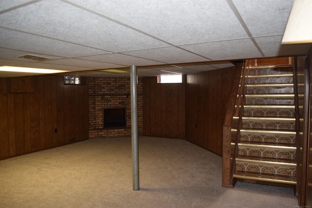 basement with visible vents, carpet floors, wooden walls, a brick fireplace, and stairs