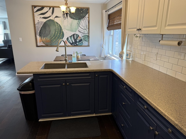 kitchen featuring dark wood-type flooring, a notable chandelier, a sink, backsplash, and light countertops