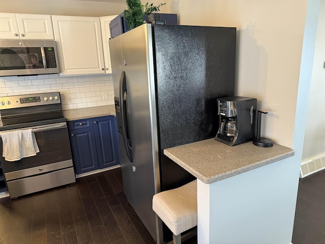 kitchen with visible vents, dark wood-type flooring, appliances with stainless steel finishes, white cabinetry, and tasteful backsplash