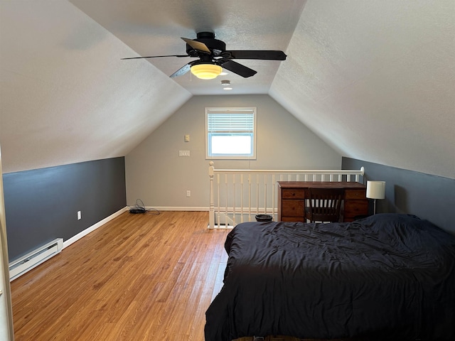 bedroom with light wood-type flooring, a baseboard heating unit, a textured ceiling, baseboards, and lofted ceiling