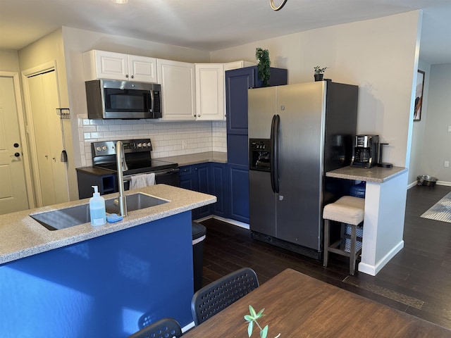 kitchen with dark wood finished floors, a sink, stainless steel appliances, white cabinetry, and backsplash