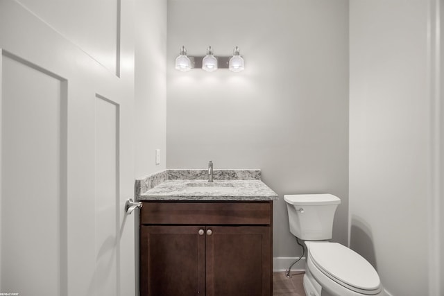 half bathroom with baseboards, toilet, and vanity