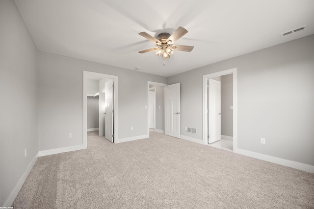 unfurnished bedroom with a spacious closet, light colored carpet, visible vents, and baseboards