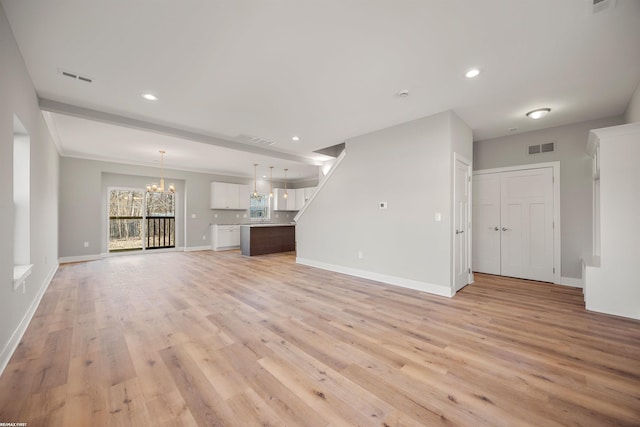 unfurnished living room with visible vents, baseboards, light wood-style floors, and an inviting chandelier