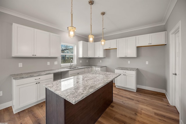 kitchen featuring a sink, light stone counters, wood finished floors, a center island, and white cabinetry