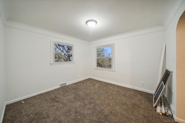 unfurnished room with arched walkways, dark carpet, and baseboards