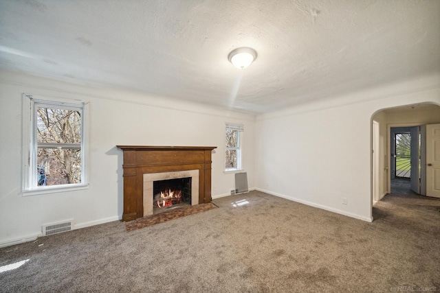 unfurnished living room featuring carpet, visible vents, arched walkways, a high end fireplace, and a textured ceiling