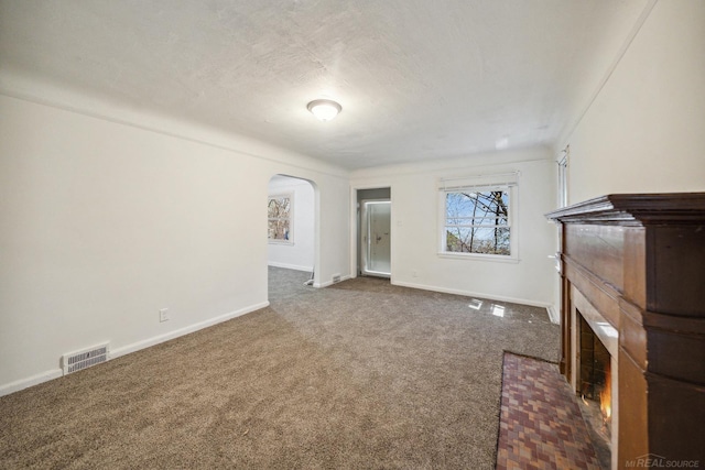 unfurnished living room with visible vents, a brick fireplace, baseboards, carpet floors, and arched walkways