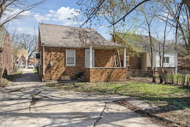 exterior space with brick siding, a shingled roof, fence, covered porch, and driveway