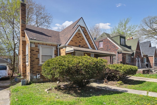 view of front of property featuring a shingled roof, brick siding, and a chimney