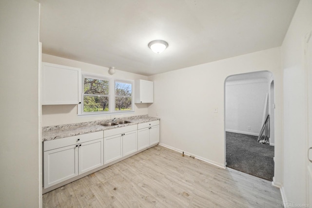 kitchen featuring baseboards, arched walkways, a sink, white cabinetry, and light wood-type flooring