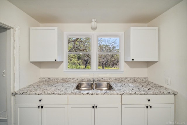 kitchen featuring a sink, light stone countertops, and white cabinetry