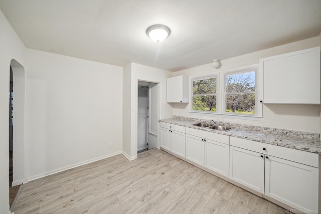 kitchen with baseboards, light wood-style floors, arched walkways, white cabinetry, and a sink