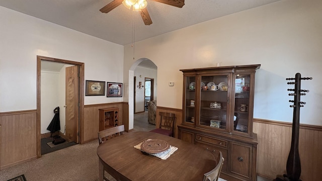 dining space with arched walkways, wainscoting, carpet, wood walls, and ceiling fan