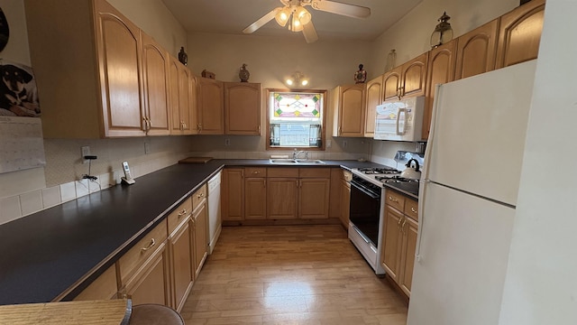kitchen featuring light wood finished floors, a sink, ceiling fan, white appliances, and dark countertops