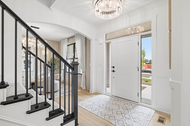17447 Megan Dr, Macomb, MI 48042 - foyer featuring arched walkways, light wood-style flooring, crown molding, a chandelier, and stairway