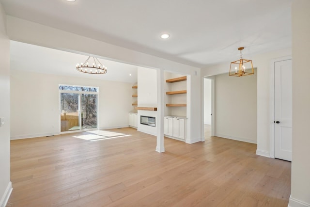 7474 Connies Dr, Shelby Twp, MI 48316 - unfurnished living room featuring baseboards, a notable chandelier, a glass covered fireplace, and light wood finished floors