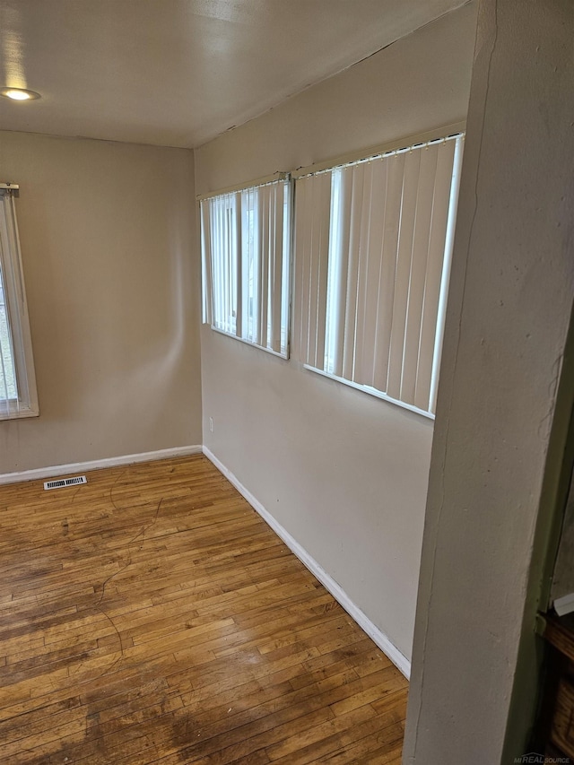 unfurnished room featuring hardwood / wood-style floors, baseboards, and visible vents