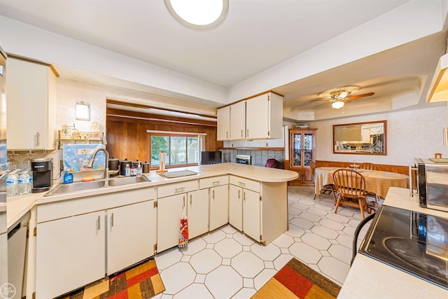 kitchen featuring light countertops, a wainscoted wall, a sink, a peninsula, and light floors
