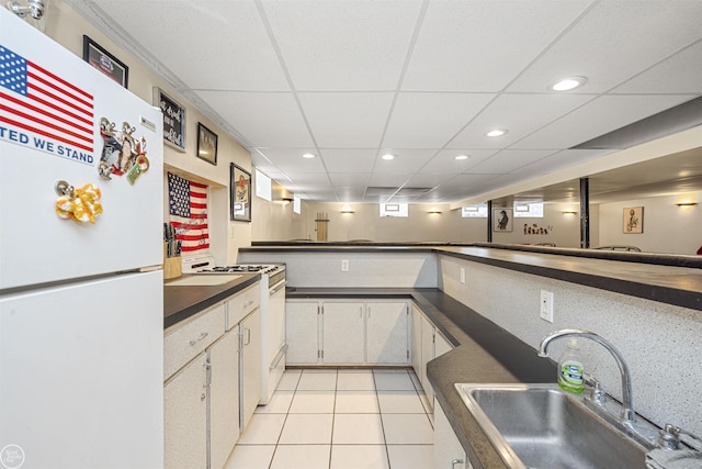 kitchen with a sink, light tile patterned floors, white appliances, dark countertops, and recessed lighting