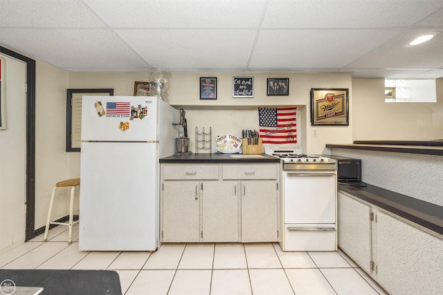 kitchen featuring light tile patterned flooring, white appliances, dark countertops, and a paneled ceiling